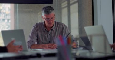 Odaklanmış orta yaşlı bir adam ofis toplantısı sırasında bilgisayardaki notları ve tipleri doğal gün ışığıyla gözden geçirir.