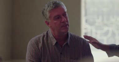 Terapi seansı sırasında, başka bir grup üyesi elini omzuna koyduğu zaman, gözleri aşağıda bir şekilde oturan bir adam, empati ve bağlantı anında destek alır.