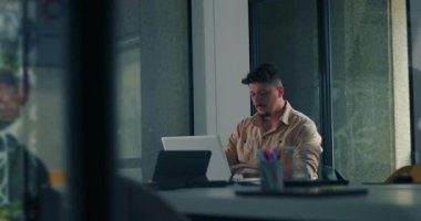Ofisteki sessiz solo çalışma sırasında dizüstü bilgisayara odaklanan genç erkek profesyonel, modern çalışma alanında doğal ışık alan bir göreve odaklanmış.