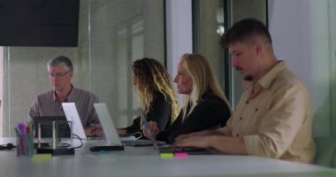 Ofis çalışanları modern takım toplantısı sırasında masa başında dizüstü bilgisayarlar açık ve profesyonel çalışma alanını dolduran doğal ışık altında odaklanmış bir sessizlik içinde çalışırlar.