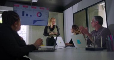 Meslektaşları profesyonel modern ofis ortamında izleme ve etkileşim kurarken sarışın iş kadını veri ekranının önünde sunum yapıyor