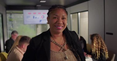 Gülümseyen Afrikalı Afrikalı Amerikalı iş kadını modern ofiste kameraya bakıyor, analitik grafik ile dijital ekranda çalışan ekip