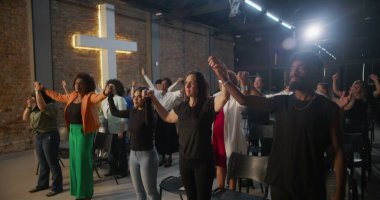 İçten bir ibadet sırasında dua ve birlik içinde el ele tutuşan cemaat, arka plandaki tuğla bir duvarda, inanç ve toplumu sembolize eden bir haç yaktı.