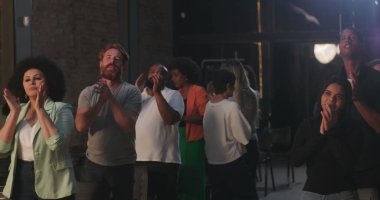 Cemaat el çırparken ve koltuklara otururken insanlar el kaldırıyor, kameralar duvardaki aydınlatılmış haça doğru dönüyor, inanç, bağlılık ve birliği ifade eden ruhani bir toplantı.