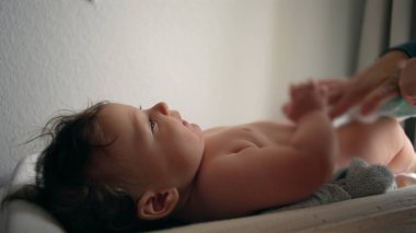 Bebek masasını değiştiriyor, anne kucağında bebek bezi, çocuk hafifçe gülümsüyor, rutin bakım, her gün ebeveyn ile etkileşim, rahatlık ve bakım, yakın ilişki..