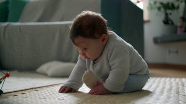 Bebek yerde oturuyor, meraklı bir ifadeyle aşağı bakıyor, rahat bir oturma odasında çevreyi keşfediyor, bağımsız, meşgul ve gözlemci olmanın ilk aşamaları..