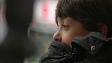 Hareket halindeki bir otobüste sessizce yansıyan genç bir çocuk, düşünceli ifadeye yakın çekim, yolculuk sırasında huzurlu bir düşünce anı