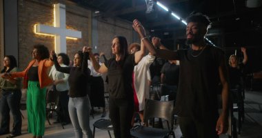 İçten bir ibadet sırasında dua ve birlik içinde el ele tutuşan cemaat, arka plandaki tuğla bir duvarda, inanç ve toplumu sembolize eden bir haç yaktı.