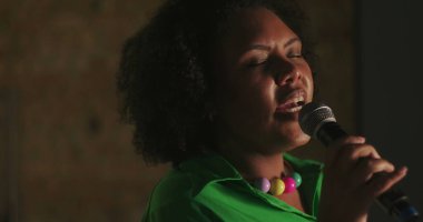 Afrika kökenli bir kadın kilise toplantısı sırasında tutkuyla şarkı söylüyor, gözleri kapalı, mikrofon tutuyor, ruhani ibadet performansı, duygusal ruhsal bağlantı