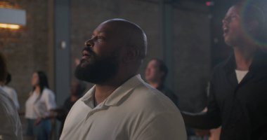 Kiliseye ibadet ederken dua eden sakallı adam, sadakat içinde elini kaldıran, arka planda aydınlanan haç ve çeşitli cemaatler, inanç ve maneviyatın ifadesi.