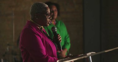 Afrika kökenli bir kadın vaaz veriyor. Evanjelik kilise toplantısı sırasında, mikrofon tutarken, güçlü vaazlar verirken, cemaate ruhani rehberlik ederken.