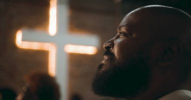 İbadet sırasında düşünceli ifadeli bir adamın profili, arka plan, inanç, maneviyat ve içgözlem konularında aydınlatılmış bir haç.