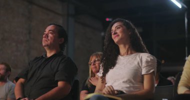 Manevi bir ortamda haçın önünde oturan bir grup insan, odaklanmış bir kadın yukarıya bakarken, diğerleri meditasyon pozunda.
