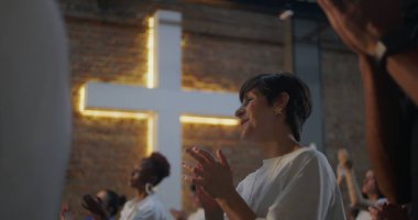 Kilisedeki çeşitli gruplar arasında el çırpan, arka planda aydınlanan haç, inanç, maneviyat ve neşe dolu bağlar.