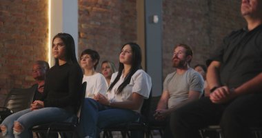 Manevi bir ortamda haçın önünde oturan bir grup insan, odaklanmış bir kadın yukarıya bakarken, diğerleri meditasyon pozunda.