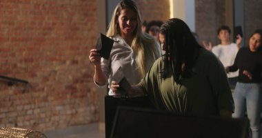 Kiliseye ibadet sırasında bağış kutusuna zarf koyan iki kadın, neşeli ve saygılı ifadeler, ruhani sunuma katılan çeşitli arka planda yer alan farklı topluluk