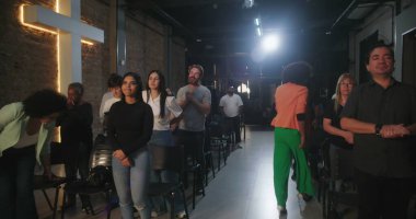 Bir Hıristiyan kilise etkinliği sırasında ayakta duran cemaat üyeleri, arka planda parlayan bir haçla ruhsal bir yansımayla meşgul oldular.