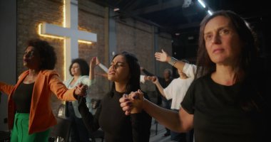 İbadet ederken el ele tutuşan, inançlarını ve bağlılıklarını ifade eden, arka planda aydınlanmış haç ruhaniliği, umudu ve yürekten birliği temsil eden bir grup insan.