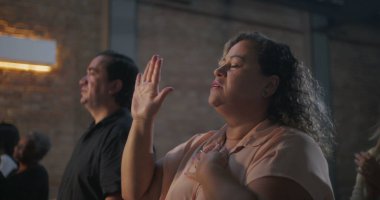 Çeşitli grup ibadetleri sırasında dua eden elleri havada, gözleri kapalı, arka planda ışık saçan kadın, maneviyat ve bağlantı vurgulandı
