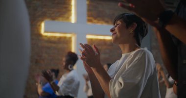 Kilisedeki çeşitli gruplar arasında el çırpan, arka planda aydınlanan haç, inanç, maneviyat ve neşe dolu bağlar.