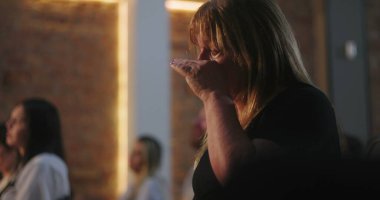 Kilisede dua ederken gözyaşlarını silen kadın, derin duygusal an, aydınlatılmış haç, ruhani yansıma, inanç, ibadet, iç huzur, inançla bağlantı