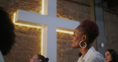 Tutkulu bir şekilde ibadet eden bir kadın, maneviyat ve inançla anlamlı ve duygusal bir bağ içinde, dua eden bir kilise cemaati ve aydınlatılmış bir haçla.