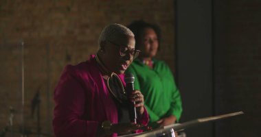 Afrika kökenli bir kadın vaaz veriyor. Evanjelik kilise toplantısı sırasında, mikrofon tutarken, güçlü vaazlar verirken, cemaate ruhani rehberlik ederken.