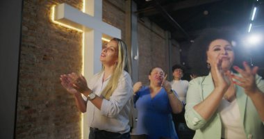 Kilisede ibadet sırasında alkışlayan ve gülümseyen çeşitli insanlar, arka planda parlayan haç, neşe, birlik ve ruhsal bağlantı ifadeleri