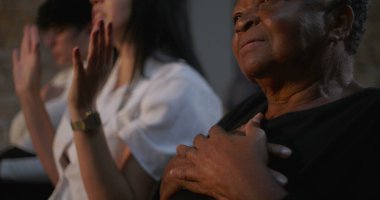 Kilisede, eli göğsünde yaşlı bir kadının yanında dua eden genç bir kadın derin maneviyat ve bağlılık, kapalı yerde dini bir toplantı, duygusal inanç anı.