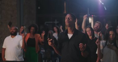 Bir grup tapan ellerinde zarflar tutarken, manevi dualarda el kaldırırken ve duygusal bir kilise toplantısında yansıtırken.