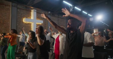 Çeşitli gruplar kilise ayini sırasında el kaldırıyor, arka planda çapraz aydınlanma, övgü, neşe ve ruhsal bağlantı ifadeleri.