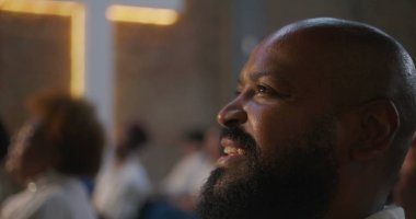 İbadet sırasında cemaatte neşeyle gülümseyen adam dingin bir kilise ortamında inanç ve maneviyatı kutluyor, parlayan yüzler ve birlik vurgulanıyor.