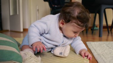 Bebek paspasın üzerinde oturuyor, ellerle çevreyi keşfediyor, merak ve odak ile dokunsal oyunlara girişiyor, ev ortamında erken çocukluk gelişimi.