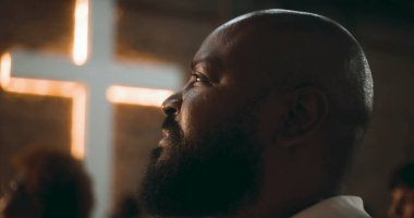 İbadet sırasında düşünceli ifadeli bir adamın profili, arka plan, inanç, maneviyat ve içgözlem konularında aydınlatılmış bir haç.