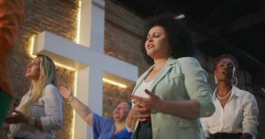 Kilisede inancın ve maneviyatın tüm kalbiyle şarkı söyleyen bir kadın, çeşitli cemaatlerle çevrili, arka planda aydınlanmış bir haç.