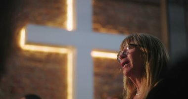Kilisede aydınlatılmış haç önünde yaşlı bir kadının portresi, dua sırasında duygusal deneyim, ruhani yansıma, inanç dolu bir an.