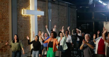 Cemaat ibadet ediyor, el kaldırıyor ve bir kilise ayini sırasında dua ediyor ve kutlama yapıyor. Masa başı olarak tuğla bir duvarda haç parlıyor.