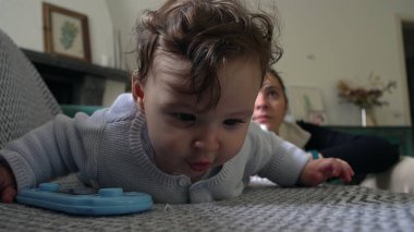 Bebek koltuğa yaslanırken mavi nesneyle oynuyor, anne arkadan izliyor, bebek keşfe çıkıyor, eğlenceli bir öğrenme anı, evde anne ile vakit geçiriyor..