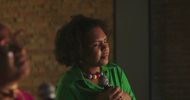 Şarkıcılar evanjelik kilise toplantısı sırasında tutkuyla şarkı söylerler, Afrikalı kökenli kadınlar mikrofon tutarlar, kalpten ibadet ederler, ruhsal ses iletimi, ruhsal bağlantı.