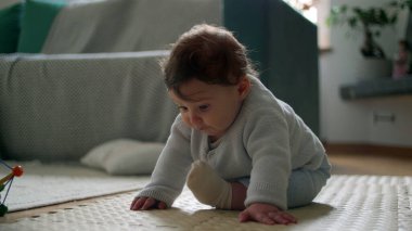 Bebek yerde oturuyor, meraklı bir ifadeyle aşağı bakıyor, rahat bir oturma odasında çevreyi keşfediyor, bağımsız, meşgul ve gözlemci olmanın ilk aşamaları..