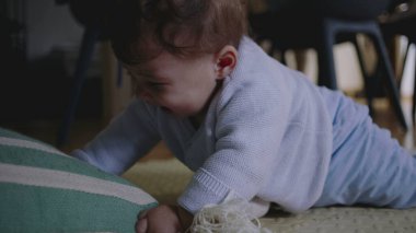 Bebek yerde yatıyor, çizgili bir yastığa uzanıyor, hayal kırıklığı ve öfke belirtileri gösteriyor, dokunarak oynamaya çabalıyor, hareket becerilerini geliştiriyor..