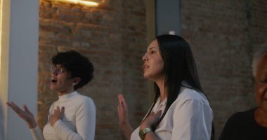 Elleri göğsünde, ibadet sırasında şarkı söyleyen ve dua eden insanlar, çeşitli cemaatlerde inanç, bağlılık ve duygusal bağlılık gösteriyorlar.