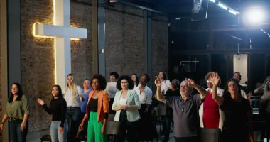 Cemaat ibadet ediyor, el kaldırıyor ve bir kilise ayini sırasında dua ediyor ve kutlama yapıyor. Masa başı olarak tuğla bir duvarda haç parlıyor.
