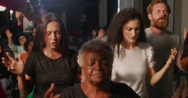 Kilisenin kutsaması sırasında diz çöken adam, ruhani lider tarafından alnına konan el, inanç ve sadakate kapalı gözler, arka planda dua eden çeşitli cemaat.