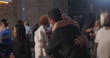 Çeşitli cemaat üyeleri modern bir kilise ortamında kucaklaşıp gülümsüyor, bir topluluk, bağlantı ve paylaşılan maneviyat duygusu yaratıyorlar.