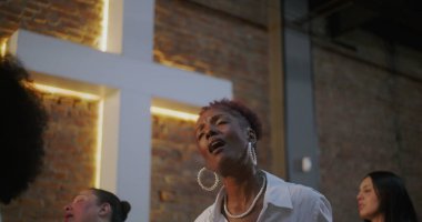 Tutkulu bir şekilde ibadet eden bir kadın, maneviyat ve inançla anlamlı ve duygusal bir bağ içinde, dua eden bir kilise cemaati ve aydınlatılmış bir haçla.