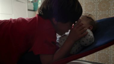 Ağabeyim bebeğin alnına hafifçe dokunurken bebek de bir fedainin içinde dinleniyor. Sıcak bir aile ortamında sevgi dolu bir kardeş etkileşimi..