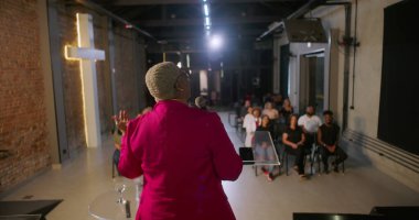 İbadet sırasında cemaate seslenen konuşmacı, izleyiciler sıraya dizilmiş, tuğla bir duvarda yanan haç dingin ve ilham verici bir atmosfer yaratıyor.