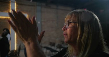 Bir kilise ayini sırasında kollar kaldırıldı, arka planda parlayan haç, kutsal bir topluluk ortamında ruhani bağlılığın, inancın ve övgülerin güçlü ifadesi.