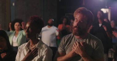 Manevi toplantı sırasında elleri göğsünde dua eden bir adam, çeşitli cemaatlerle çevrili, yanında dua eden Afrikalı Amerikalı bir kadın, inanç ve bağlılık vurgulandı